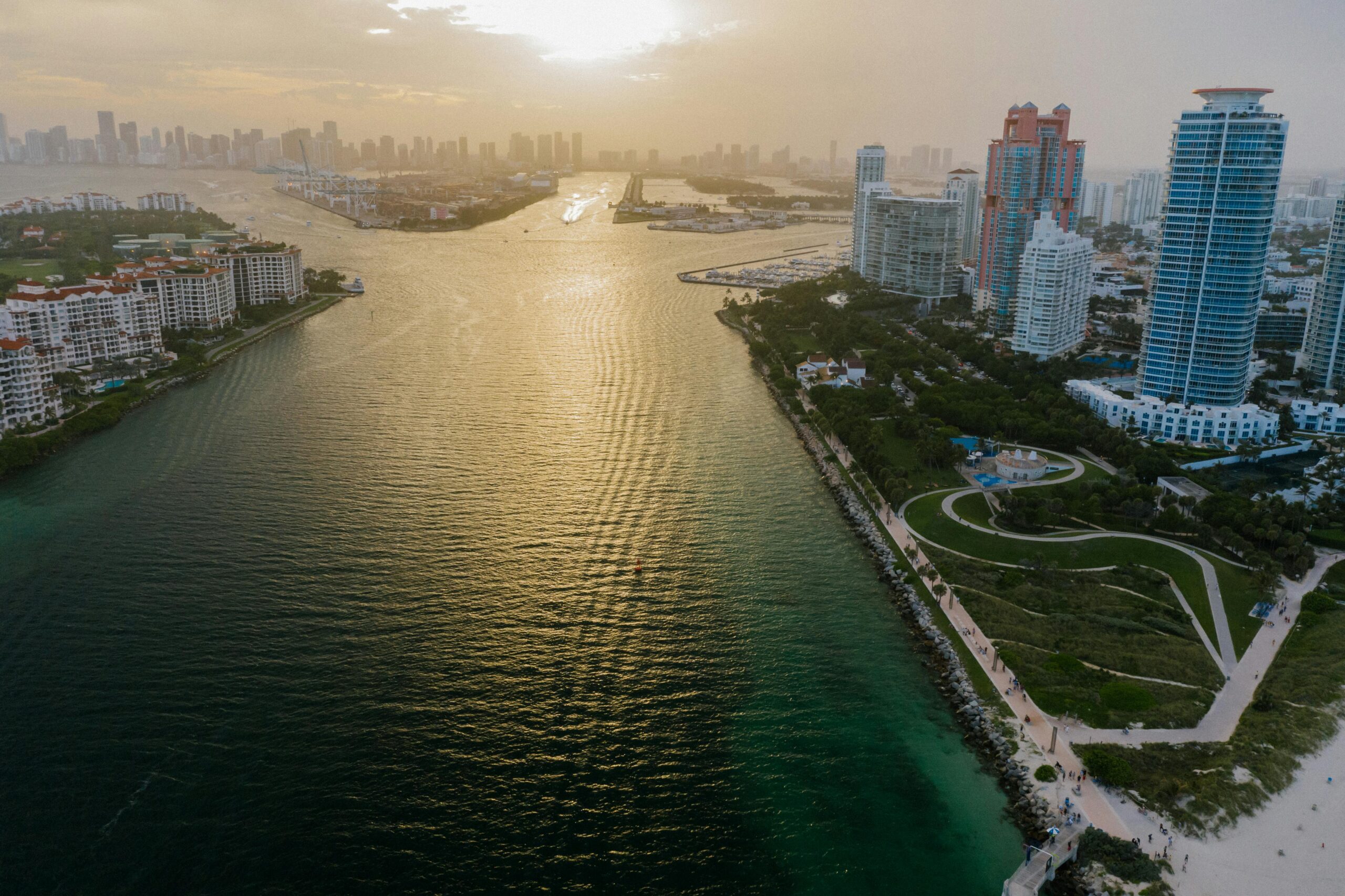 Aerial view of Miami skyline and waterfront at sunset with golden light on the water.